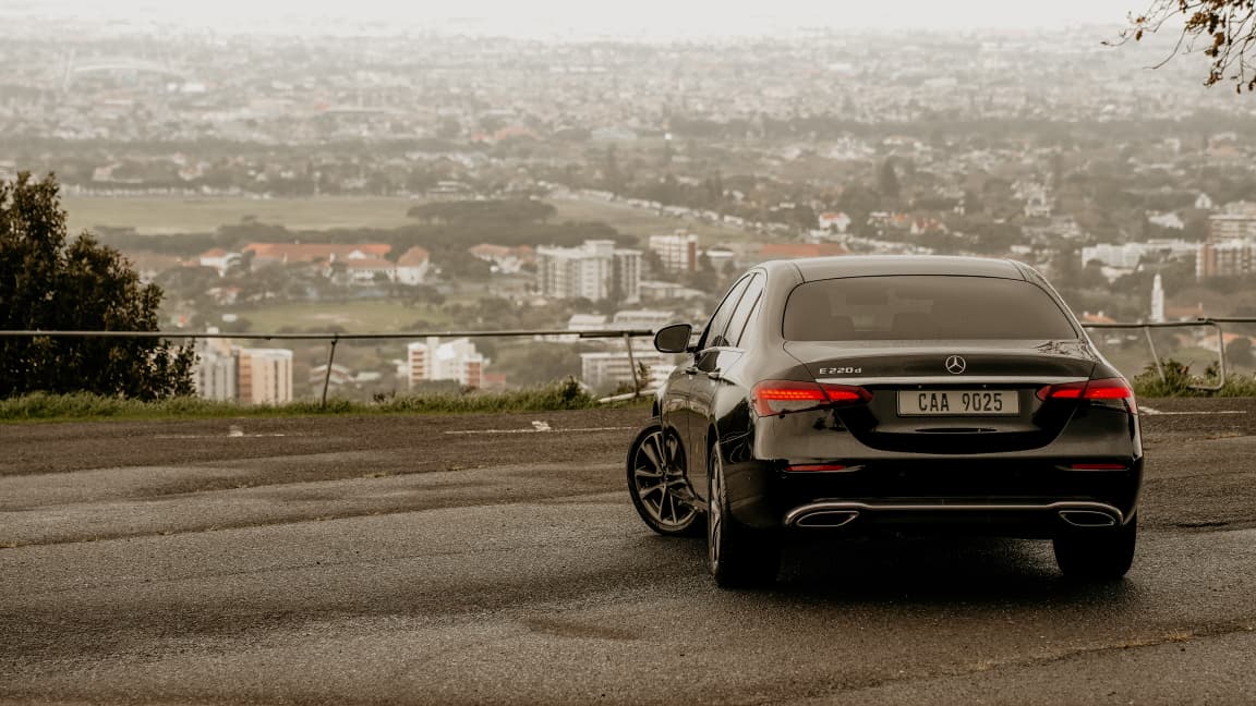 Black Mercedes-Benz E-Class rear profile on a Cape Town overlook road